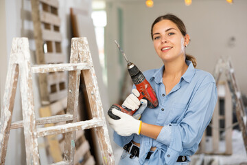 Portrait of smiling young woman with drill in apartment during renovation works. - obrazy, fototapety, plakaty