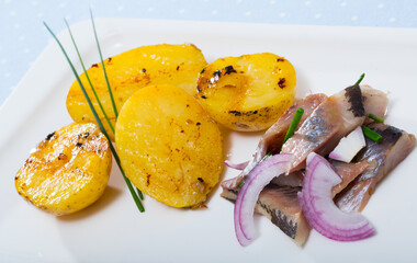 Slices of pickled herring with pieces of roasted potatoes and herbs served on plate