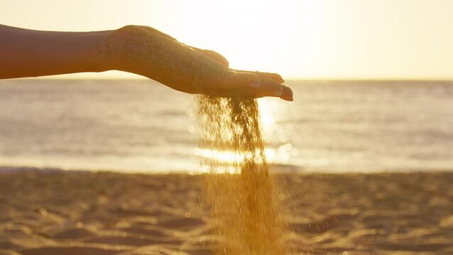 RED camera slow motion close up Unknown young woman throws handful of shiny golden sand at sunset background. Girl on summer holiday on Hawaii Islands plays on stunning tropical beach at scenic light