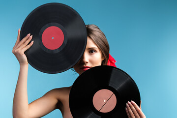 Beautiful lady naked with red ribbon on the hair tail and make up holding two vinyl music records covering part of her face.