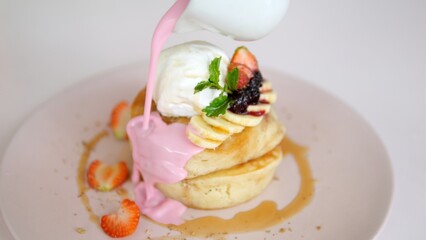 Close-up of an appetizing breakfast of sweet pancakes with fruits and berries poured over with a delicious cream. On top of the fritters is a ball of ice cream. Sweet morning mood.