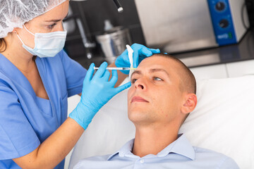 Young male patient getting injections for face skin tightening at aesthetic cosmetology clinic