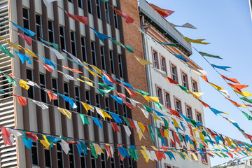 Colorful bright flags are strung on threads. Colored flags on the background of the sky and city buildings. Small flags over the square are flying in the wind. A holiday on a sunny day on the streets 