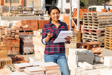 Concentrated hispanic woman worker controlling quantity of tiles at hardware store warehouse