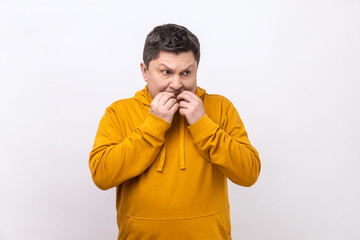 Nervous terrified middle aged man biting his fingers with shocked look, fears and phobias, looking away, wearing urban style hoodie. Indoor studio shot isolated on white background.
