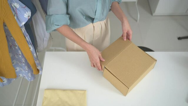 Asian beautiful woman packing a clothes into a parcel cardboard box for shipping.
