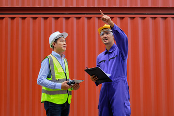 Two professional Asian male workers in safety uniforms and hard hats on a steel container background, work at logistics terminal, loading control shipping goods for the cargo transportation industry.