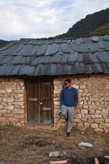 Short hair guy standing against old structure wall made of stone and mud looking his right side and wearing black sunglasses