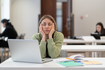 Exhausted middle-aged woman student sitting with closed eyes at desk with laptop in classroom,...