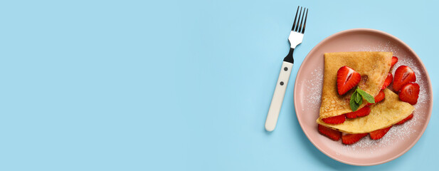 Plate of thin pancakes with strawberry and fork on blue background with space for text
