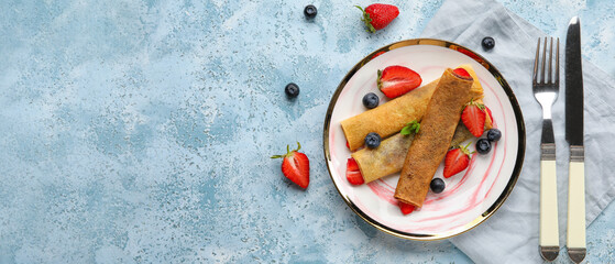 Plate of thin pancakes with berries and cutlery on blue grunge background with space for text