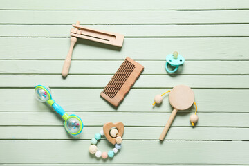Baby hair comb and different accessories on green wooden background