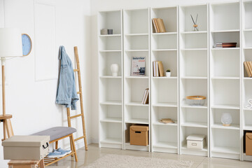 Stylish shelf unit with books and decor near white wall