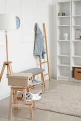 Stylish shelf unit and soft bench with shoes near white wall