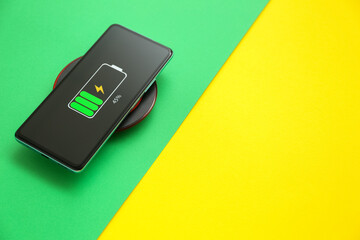 Modern mobile phone charging with wireless pad on color background