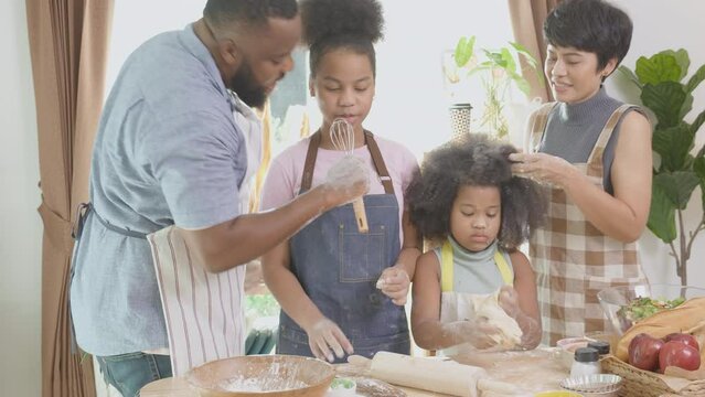 African America family wearing apron thresh flour for cooking and dancing and song together in the kitchen at home, parent and little child preparing food and song with fun and playful.