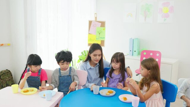Asian young female teacher take care young kids student having lunch.