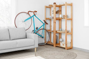 Interior of light living room with bicycle, grey sofa and wooden shelving unit