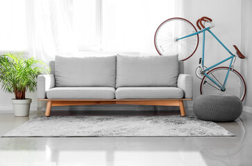 Interior of light living room with bicycle, grey sofa and pouf