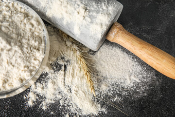 Bowl with wheat flour and rolling pin on dark table, closeup