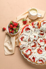 Baking dish with strawberry cinnamon rolls, cream and napkin on beige background