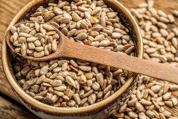Bowl and spoon with peeled sunflower seeds on wooden background, closeup