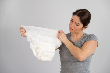 A caucasian woman holds an adult diaper and checks its strength on a white background. 