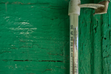 On the green-painted wooden wall of a village house, the thermometer reads 33 degrees Celsius. Summer, heat, global warming.