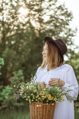 portrait of a happy girl with short hair in a black hat with a basket of flowers walking in a field