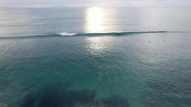 People try to catch mediocre waves, aerial shot of Dreamland beach surf zone at sunny evening. Wave grow and move towards, but quickly crumble to white-wash, yet one person can make the short ride