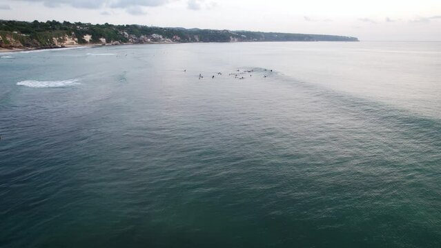 Group of surfers wait together on water and then catch the wave, do very short ride before it crumble down to whitewater. Aerial shot of ocean surf zone at Dreamland beach, South Kuta, Bali island