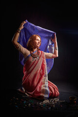 A beautiful European woman in a traditional Indian sari on a black background. Girl model posing in the studio