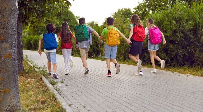 Happy students on their way to school. Group of children running to class. Several kids with colorful backpacks running along the park path together. Back to school concept. Backside view from behind