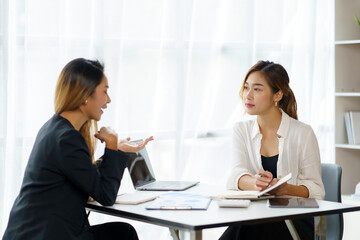 Two young Asian professional businesswomen working talking in a modern startup.