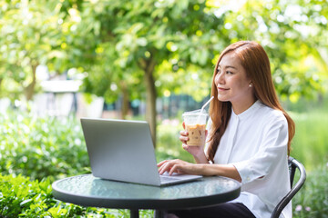 Portrait image of a young businesswoman drink coffee while working on laptop computer in the outdoors