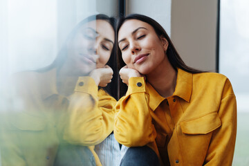 Young woman leans relaxed on the window and has her eyes closed - Powered by Adobe