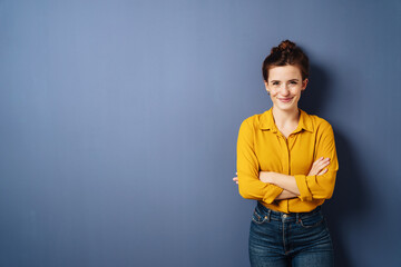 young woman with folded arms looks smiling into the camera, copy space on blue background