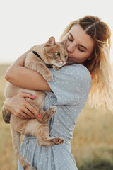 Caucasian Young Woman Dressed in Blue Dress Holding Her Red Cat Outdoors at Sunset
