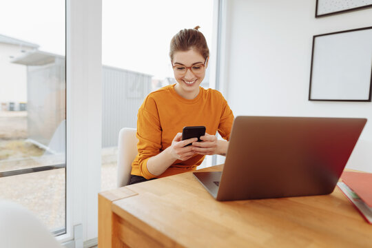 young woman in home office with cell phone and laptop