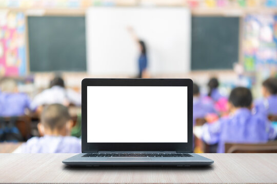 Computer on the table, blur image of children in the classroom as background.