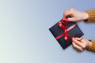 Flat lay of woman hands holding gift wrapped and decorated with bow on blue background with copy...