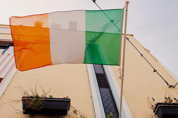 National flag of Ireland mounted on a wall of a light yellow building. Irish tricolor in town.