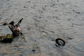 Stolen and dumped in a river bicycle. Criminal and environment issue. Dirty bike in water in town urban area.