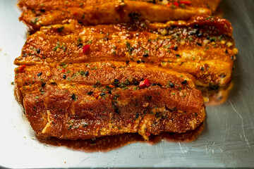 Raw uncooked pork belly marinated in Asian style with herbs and spices on a metal tray. Meat industry and product known for tenderness and great flavor. Summer range meat. Close up