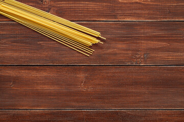 Spaghetti raw, long pasta, on wooden brown plank tabletop background, top view, space to copy text.