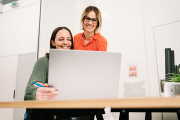 two colleagues laughing together looking at the laptop in the office