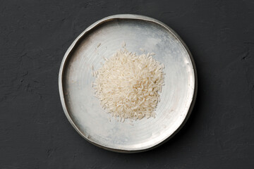 Heap of dry rice in a bowl on black background, lack of food, hunger concept
