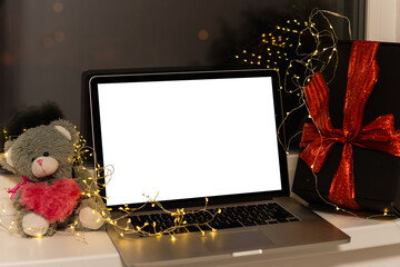 Laptop computer with white blank empty mock up screen on Merry Christmas table with presents gifts boxes in warehouse background. Ecommerce website xmas online shopping and shipping delivery, banner