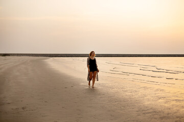 Beautiful girl strolls along the beach by the ocean at sunset