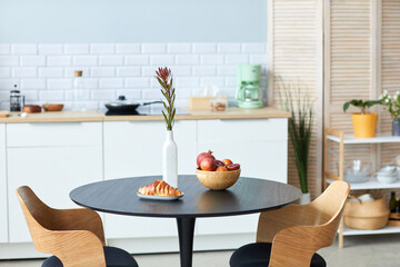 Closeup of fruit and croissants on elegant table and chairs set in wood with black detail in minimal kitchen interior, copy space